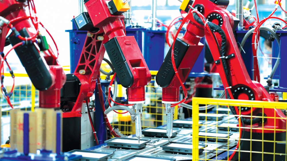 The image shows a highly automated factory floor with several red, robotic arms assembling products.AI-generated content may be incorrect.